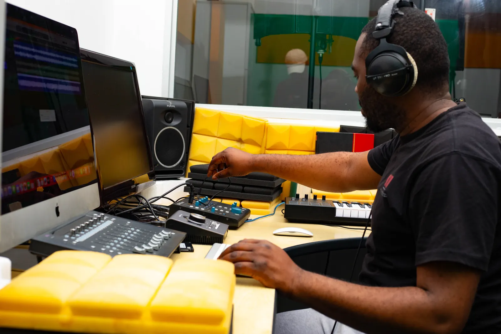 Engineer working at the keyboard in the SN7 control room, with yellow acoustic treatment behind the desk.