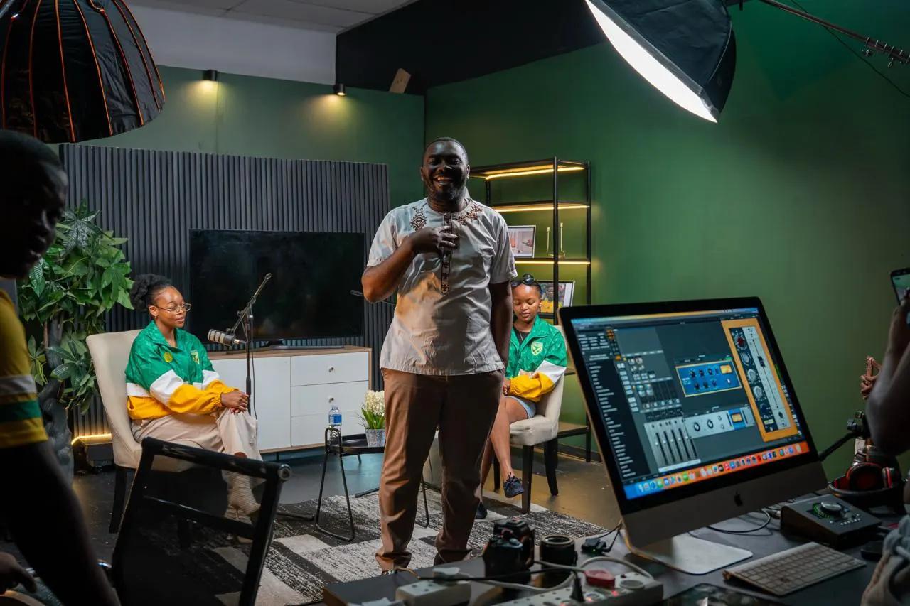 A filmed studio session in progress, with lights, guests, and the control desk in front.
